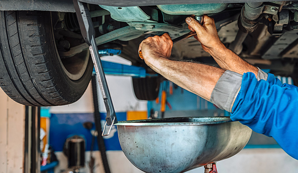 A mechanic draining oil from a car into a pan