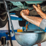 A mechanic draining oil from a car into a pan