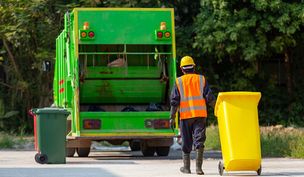 A man in high visible clothing taking a yellow bin to a garbage disposal truck