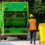 A man in high visible clothing taking a yellow bin to a garbage disposal truck