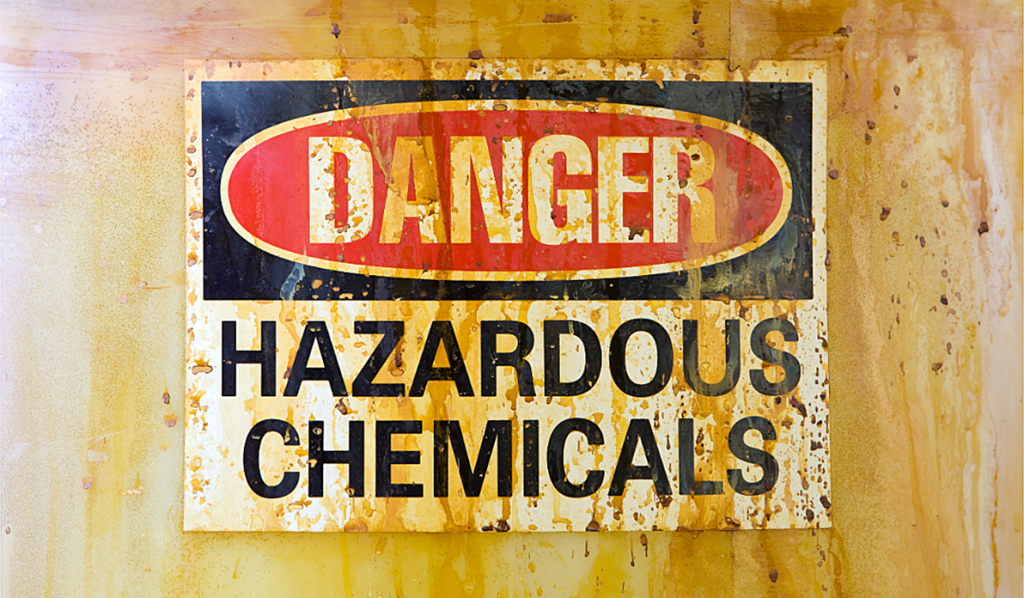 Weathered warning sign reading “Danger Hazardous Chemicals” mounted on a stained industrial surface, highlighting the risks associated with hazardous chemical handling and storage.