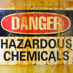 Weathered warning sign reading “Danger Hazardous Chemicals” mounted on a stained industrial surface, highlighting the risks associated with hazardous chemical handling and storage.