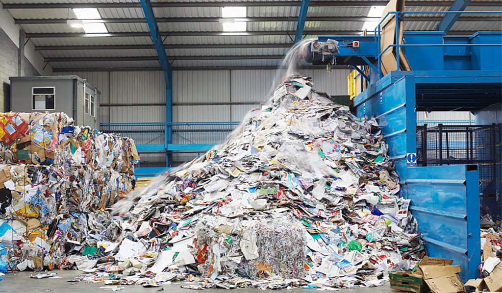 Large pile of mixed paper and cardboard materials being processed at a recycling facility.