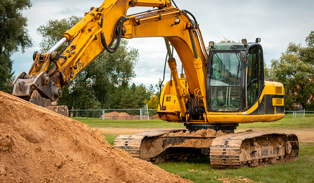 Yellow excavator moving a pile of soil at a construction site.