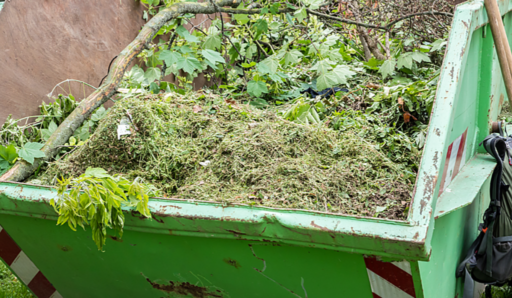 Green skip bin filled with garden waste, including grass clippings, leaves and branches.